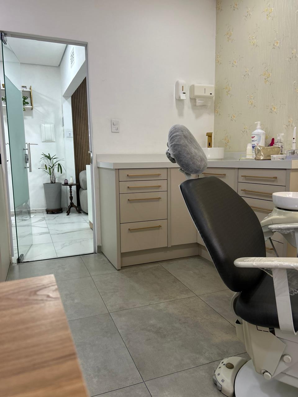 Consultório com cadeira odontológica, armários claros e puxadores dourados